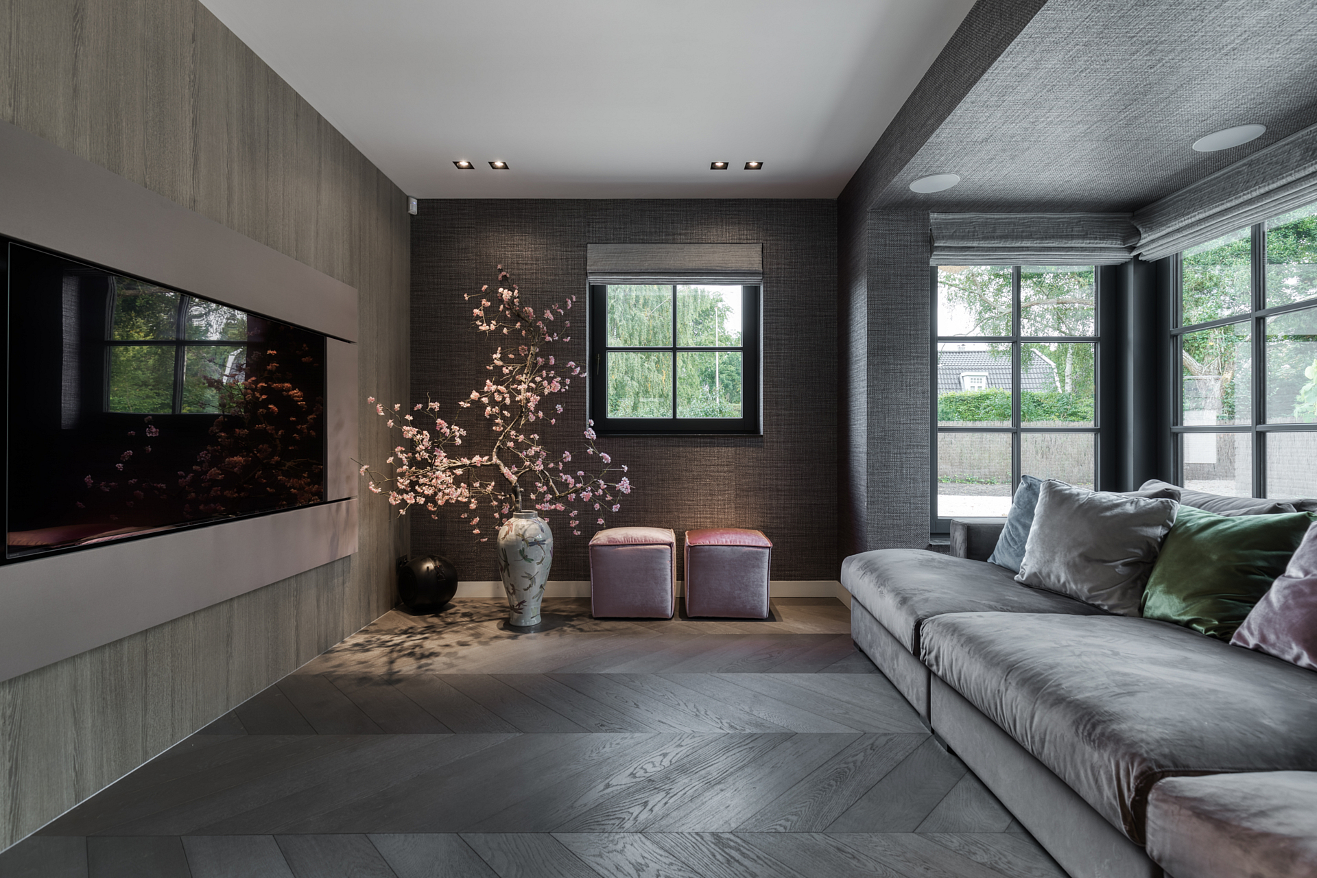 Home cinema corner with comfortable grey sofa, blossom decoration and fabric wallpaper