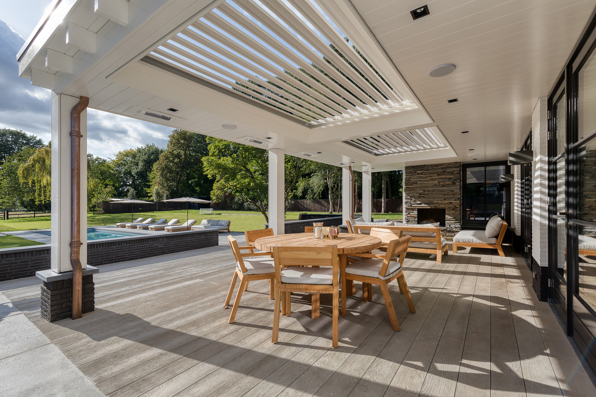 a backyard deck with sunbathed wood and overhanging automatic shutters looking out over the pool