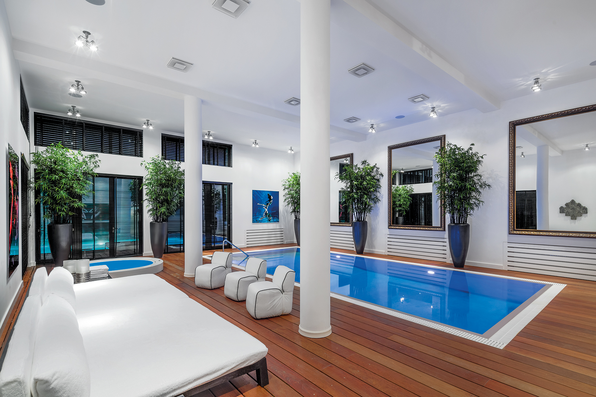 Indoor pool with surrounding deck and a Jacuzzi in the corner. Large mirrors and potted bamboos line the wall